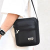 Black water-resistant multi-pocket crossbody chest bag with a zipper and a silver logo on a white shirt.