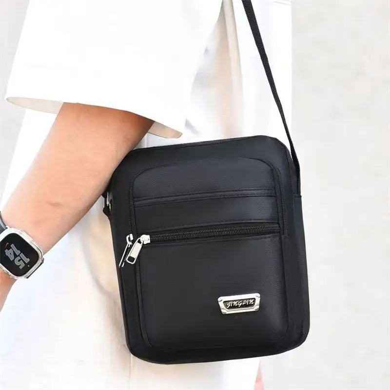 Black water-resistant multi-pocket crossbody chest bag with a zipper and a silver logo on a white shirt.