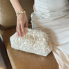 A hand places a white sequin beaded chain shoulder clutch bag on a brown leather sofa.