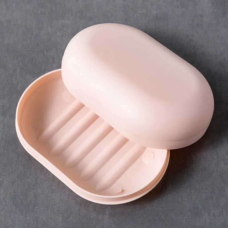 A pink portable soap dish with a lid is shown, featuring ribbed compartments for holding soap.