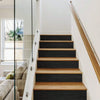 A modern interior staircase with dark wood treads and black risers, next to a glass door and window.