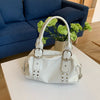 A white soft PU leather shoulder bag with silver rivet accents resting on a white table.
