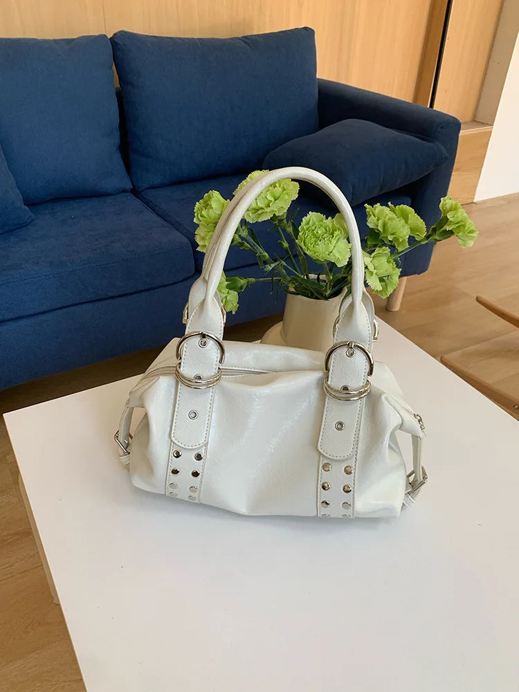 A white soft PU leather shoulder bag with silver rivet accents resting on a white table.