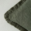A close-up of a sage green linen throw pillow cover with dark fringe.