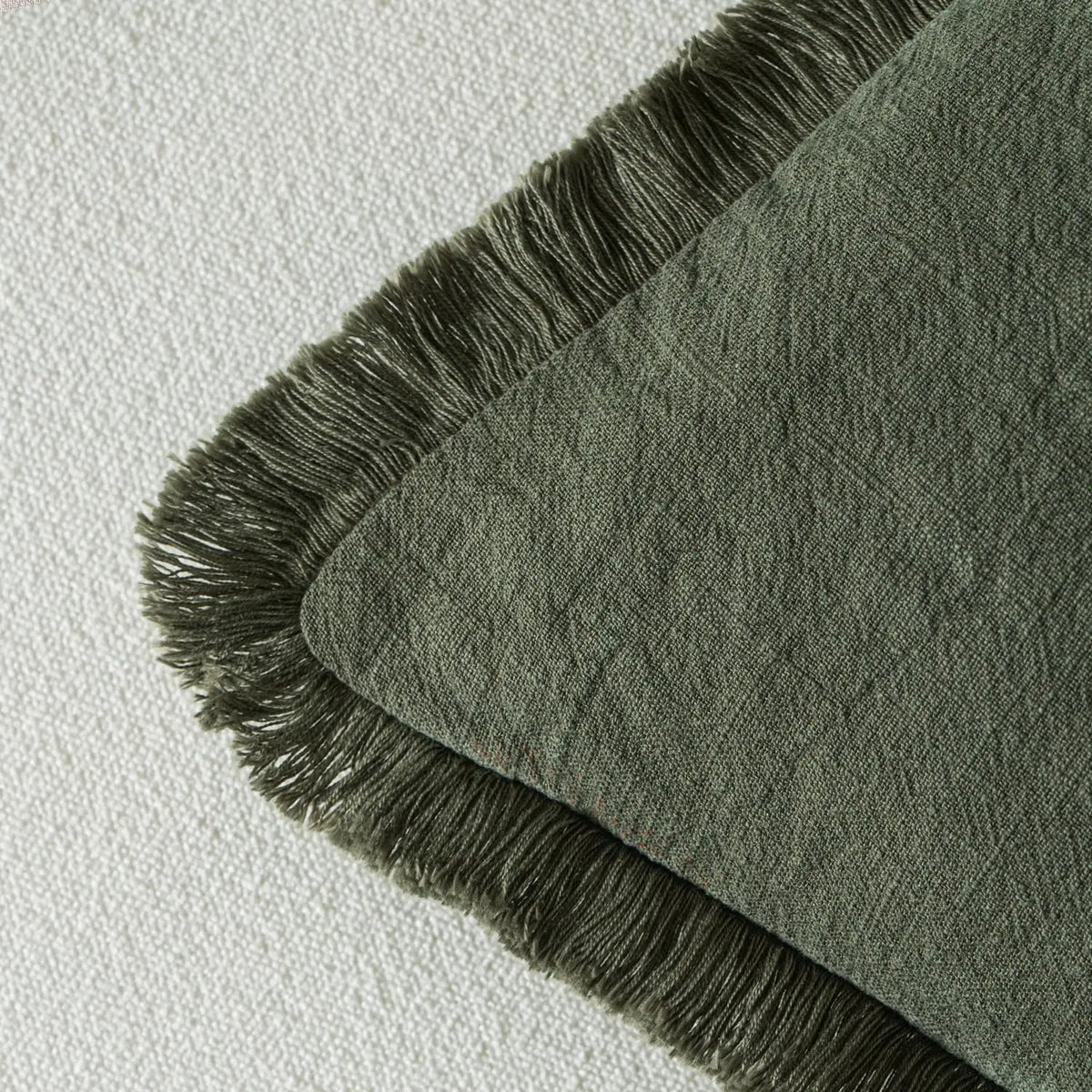 A close-up of a sage green linen throw pillow cover with dark fringe.