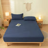 A dark blue fitted bed sheet set with matching pillowcases displayed on a wooden bed frame in a bright bedroom.