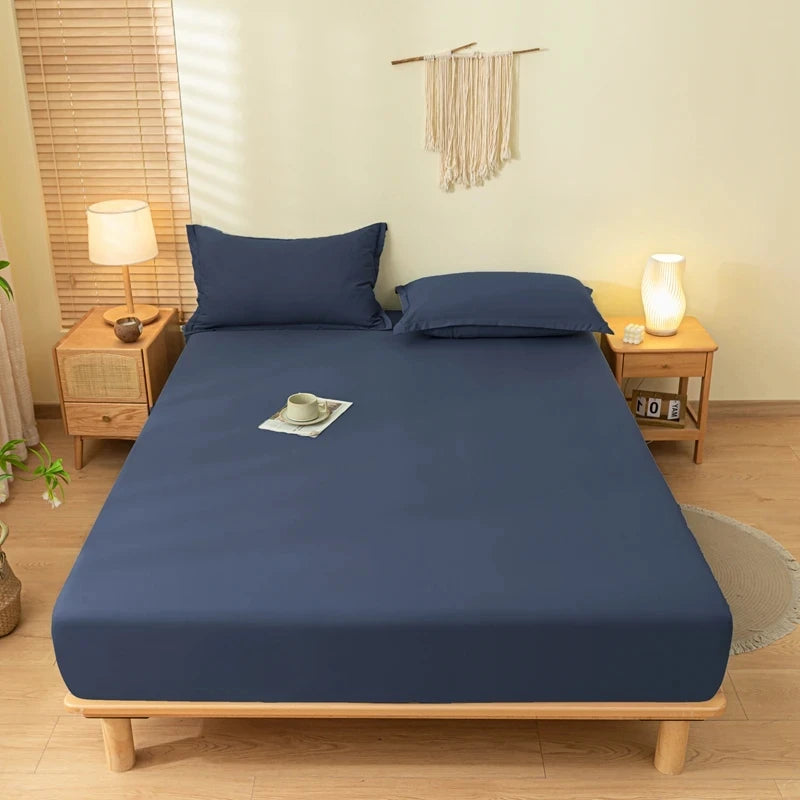 A dark blue fitted bed sheet set with matching pillowcases displayed on a wooden bed frame in a bright bedroom.