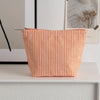 Pochette en tissu rayé orange et blanc posée sur une surface blanche.