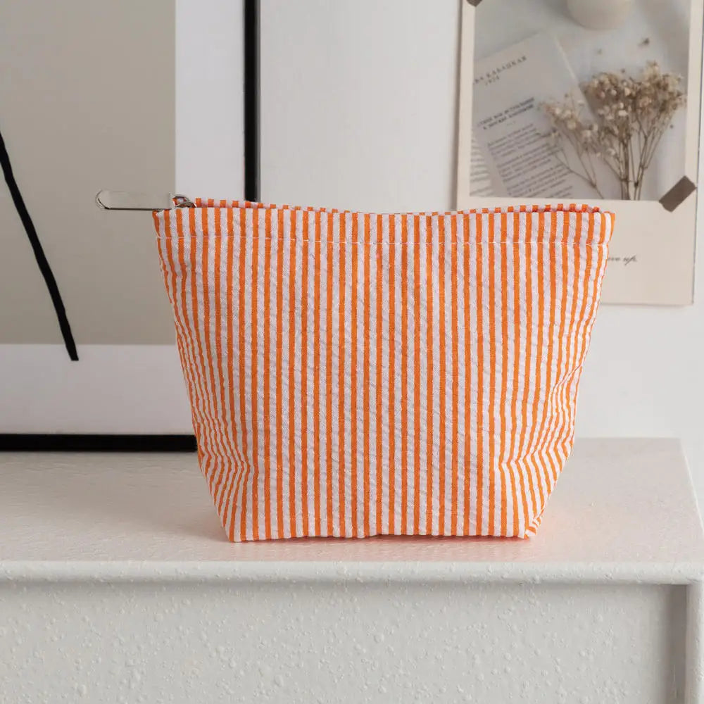 Pochette en tissu rayé orange et blanc posée sur une surface blanche.