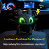 A black Toothless car ornament with glowing green eyes and movable wings displayed on a car dashboard.