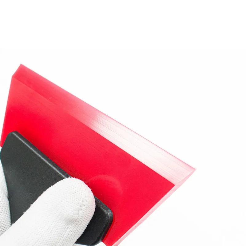 A red car windshield ice scraper and squeegee held by a white glove.