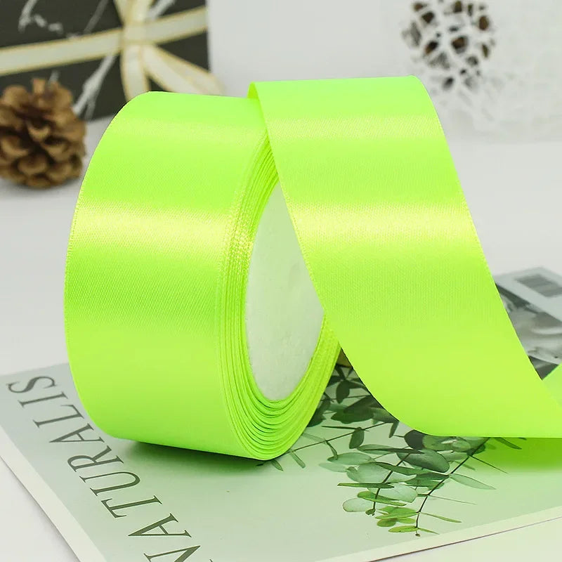 A roll of bright lime green satin ribbon shown unwrapped on a light green surface.
