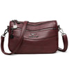 A maroon leather compact square crossbody bag with gold hardware and a zipper detail.