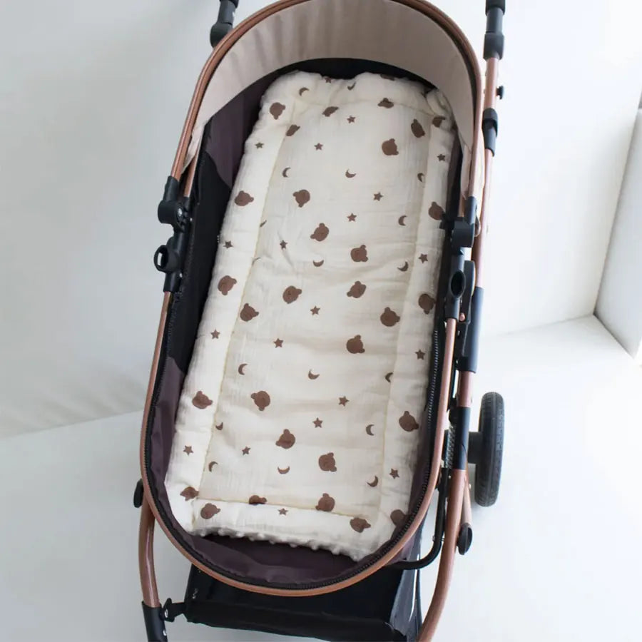 A beige and brown cartoon bear stroller cushion is shown inside a brown stroller basket.