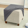 A gray stretch jacquard ottoman slipcover draped over a light beige upholstered ottoman.