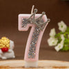A pink candle shaped like the number seven decorated with a silver rhinestone crown.