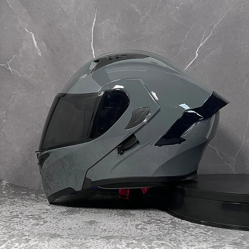 A dark gray DOT-approved modular flip-up motorcycle helmet resting on a gray textured surface.