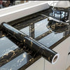 Black marble wall sticker roll with gold veining displayed on a kitchen countertop.