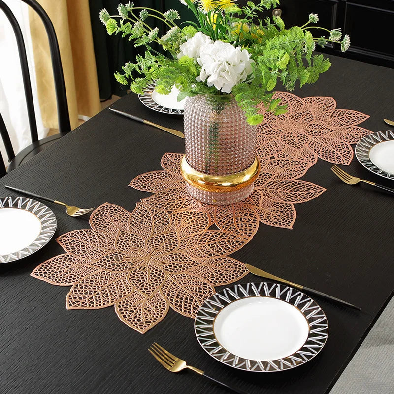 A black table set featuring ornate copper-colored floral placemats, plates, and silverware with a centerpiece of white flower