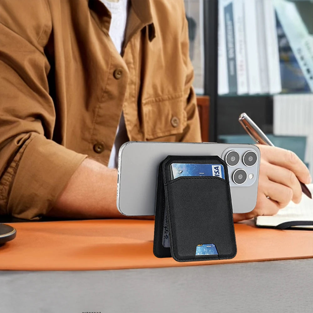 A hand holds a black magnetic leather wallet case for an iPhone with a card holder on an orange desk.