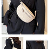 A woman wearing a black blazer holds a cream-colored multi-pocket PU leather waist bag with a silver chain strap.