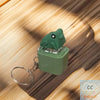 A green interactive fidget keychain featuring a plastic frog with sound and LED lights resting on a wooden surface.
