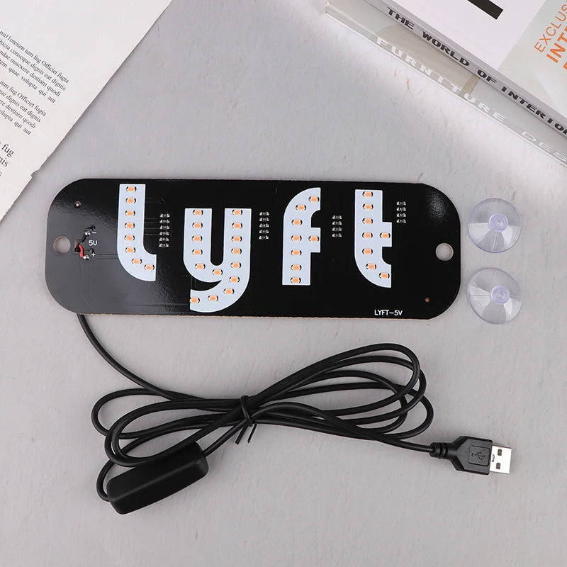 A black USB-powered LED taxi sign with letters LYFT mounted on a white background and connected by a black wire.