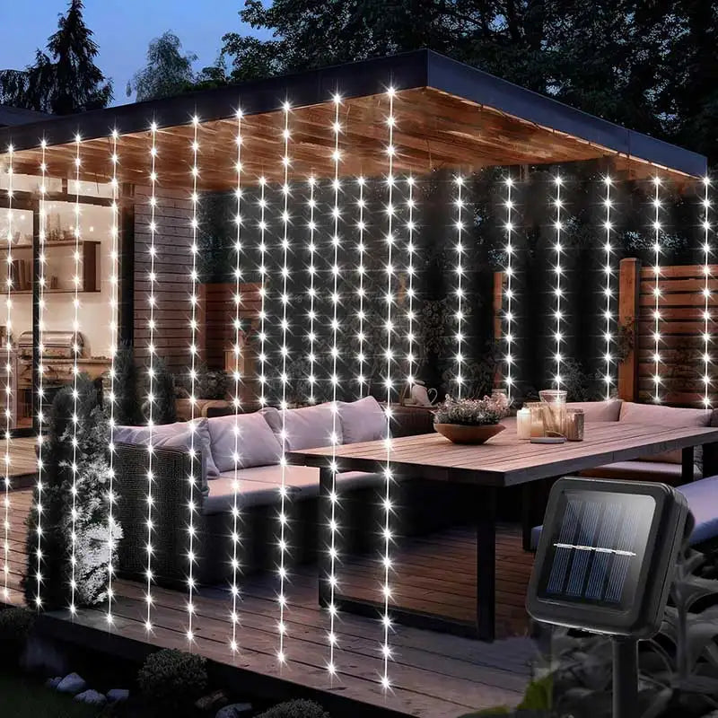 Outdoor curtain lights illuminating a wooden deck and greenery at dusk.
