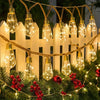 String lights with amber glass bulbs are strung across a white picket fence and decorated with red berries.