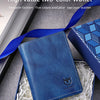 A dark blue leather wallet is shown inside a box with shredded paper, next to a blue ribbon and some metal keys.