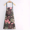 A floral print kitchen apron in shades of pink, green, and gray hanging on a wooden hanger.