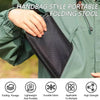A hand holds a black folding stool designed as a handbag style portable outdoor seat.