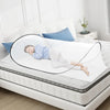 A transparent dome-shaped mosquito net is shown resting on a white bed, illustrating its pop-up design.
