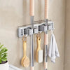 Wall-mounted metal holder for mop and broom with detachable hooks, featuring pink and silver poles.