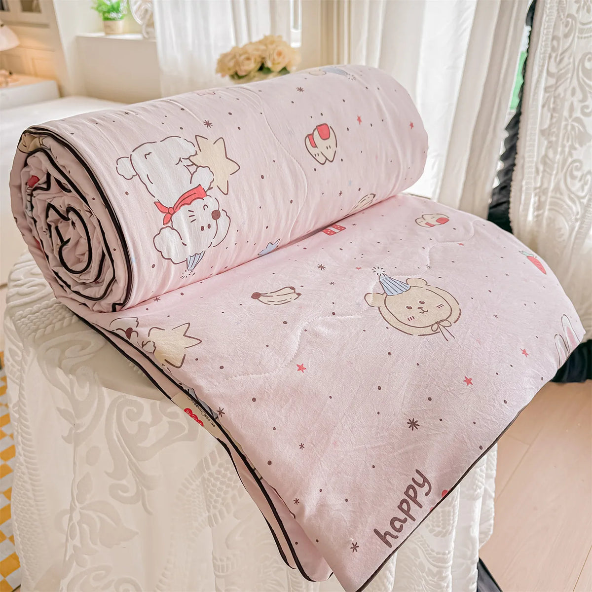 A pink embroidered pillow featuring a white bear and stars with the word happy on a white lace surface.