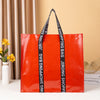 A bright orange leather shopping bag with black straps displayed against a beige background.