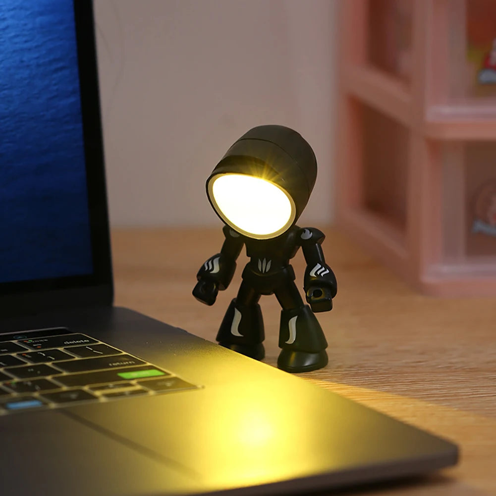A small black robot night light with a glowing face sits on a laptop keyboard.