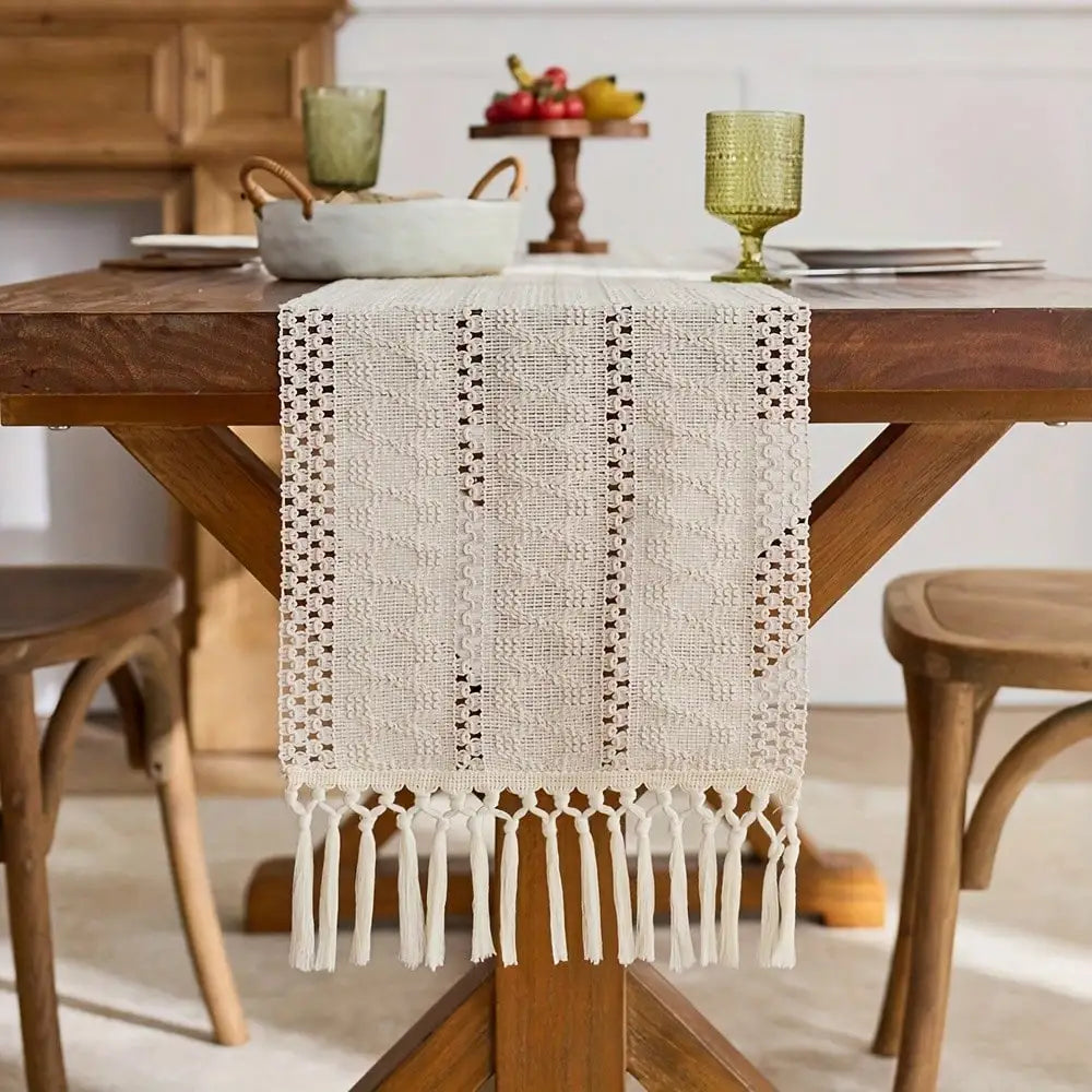 Beige tasseled table runner with macrame detailing on a wooden dining table.