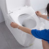 A person is installing a white disposable toilet seat cover onto a toilet bowl.