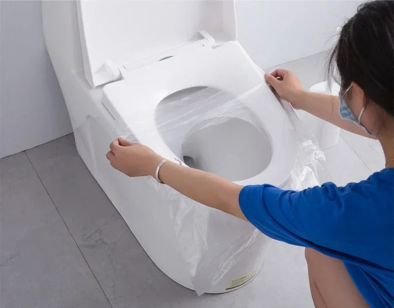 A person is installing a white disposable toilet seat cover onto a toilet bowl.