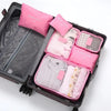 A black travel packing cube case filled with six pink laundry pouches and a pink pillow.