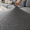 A hand is adjusting a gray jacquard fleece sofa cover with an anti-slip backing on a sectional sofa.