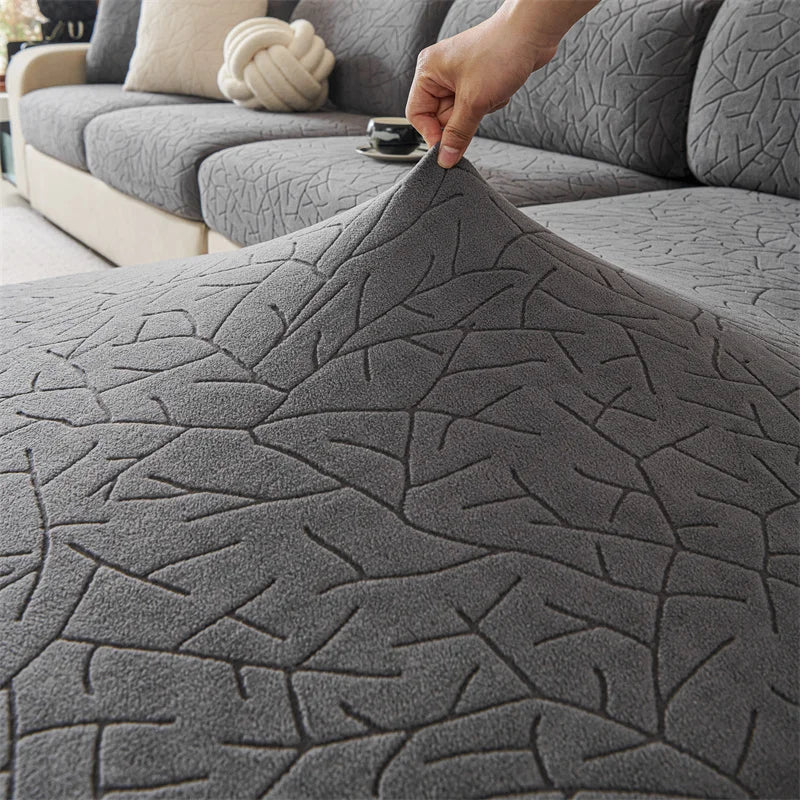 A hand is adjusting a gray jacquard fleece sofa cover with an anti-slip backing on a sectional sofa.