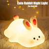 A white rabbit night light with pink ears glowing softly on a fluffy surface.