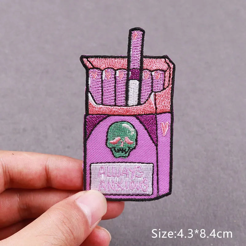 A pink embroidered patch featuring a skull design and a straw, shown being held by a hand.