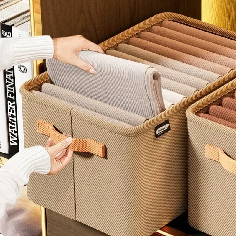 A hand is opening a beige fabric storage box filled with rolled, light-colored textiles for closet organization.