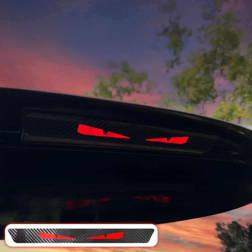 A close-up of a black car's rear light featuring a red cartoon devil eyes decal.