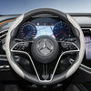 Close-up view of a black steering wheel with carbon fiber texture covers and a Mercedes-Benz logo.