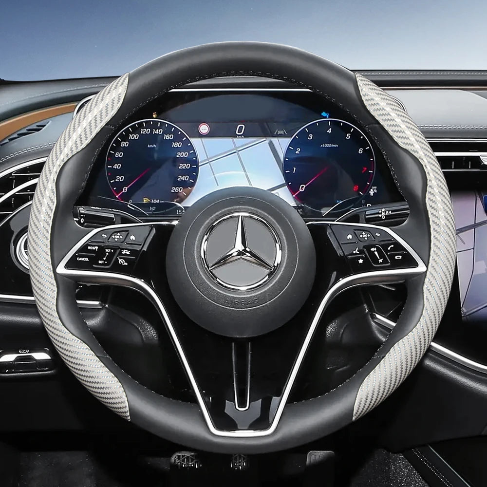 Close-up view of a black steering wheel with carbon fiber texture covers and a Mercedes-Benz logo.
