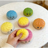 A hand holds a yellow squishy stress relief toy next to several colorful, squishy, egg-shaped toys on a white table.